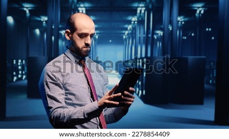 Data center IT engineer standing in server room with rack cabinets, inspecting cloud computing big data service. System administrator running networking backup on tablet, artificial intelligence.