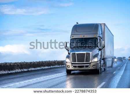 Industrial long hauler big rig gray semi truck tractor with extended cab for truck driver rest transporting cargo in dry van semi trailer driving on the twilight highway road with rain dust Royalty-Free Stock Photo #2278874353