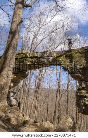 A hiker walks across the top of the arch of the natural stone bridge in Sewanee , Tennessee. The bridge is a portion of the Black Cove Trail in the south Cumberland Mountains. Winter. 