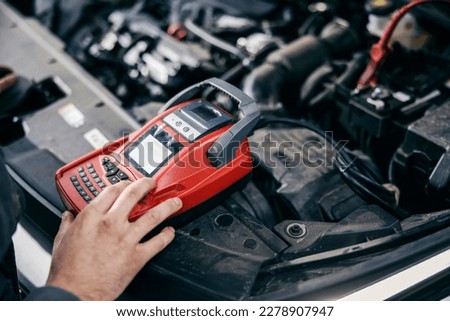 Cropped picture of a auto-mechanic's worker hand doing car battery diagnostics with device at garage.