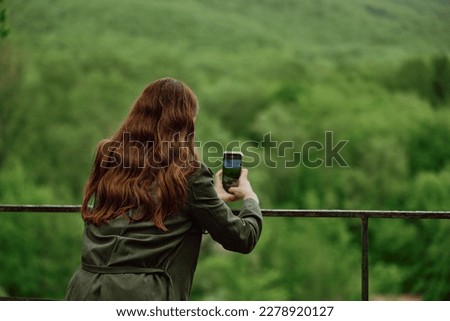 a woman in a raincoat takes pictures on the phone of a beautiful view of the forest. Travel, technology, mobile photography