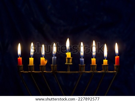 Hanukkah menorah (nine-branched candelabrum) with burning colored candles on a dark blue background