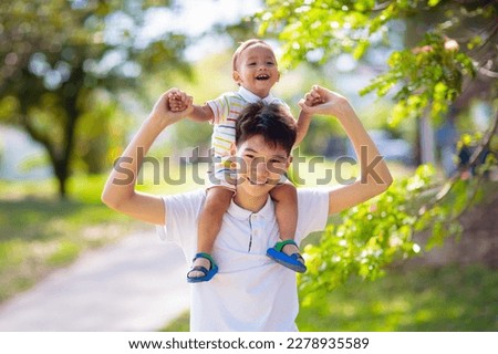 Teenage Asian boy playing with his baby brother. Brothers have fun in summer park. Siblings with big age difference. School child hugging little sibling. Kids bonding and love. Royalty-Free Stock Photo #2278935589