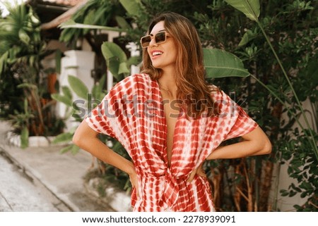 Outdoor fashion portrait of  brunette young woman posing near palm trees and wearing modern trendy outfit .  tropical vacation mood.