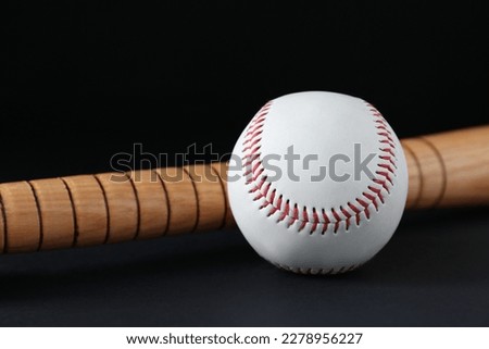 Wooden baseball bat and ball on black background, closeup. Sports equipment