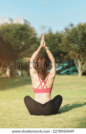 Young adult female in sportswear doing Yoga in the park outdoor, healthy woman sitting on grass and meditation with lotus pose in morning. wellness, fitness, exercise and work life balance concepts