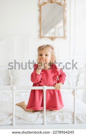 Little girl in pink dress having fun on the bed in the bedroom
