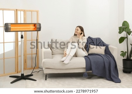 Woman warming near electric infrared heater indoors Royalty-Free Stock Photo #2278971957