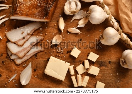 still life of food in a rural style on a dark wood background, sliced lard and garlic, cheese and onion, concept of fresh vegetables and healthy food