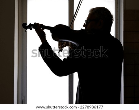 Silhouette of a violinist on the background of the window.