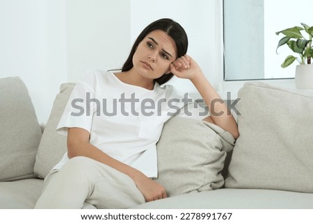 Depressed young woman sitting on sofa indoors. Hormonal disorders Royalty-Free Stock Photo #2278991767