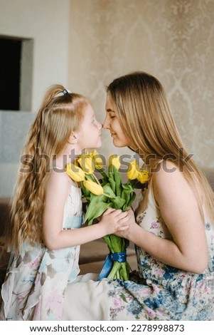 Mother's day concept. Girl congratulates mother and gives a bouquet of yellow flowers tulips at home. Mom and daughter smiling and hugging. Holiday greeting card for International Women's Day. Closeup