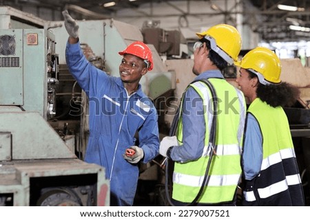 Technician engineer in protective uniform with hardhat standing and teaching apprentices or colleague worker to use computerized machine control at heavy industry manufacturing factory
