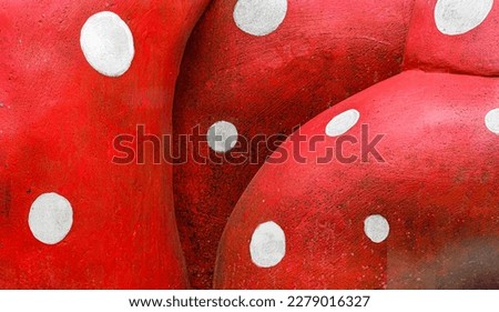 Modern sculpture of bright red dirty cement bulging boulders with white painted dots all over. Cartoon appearance.