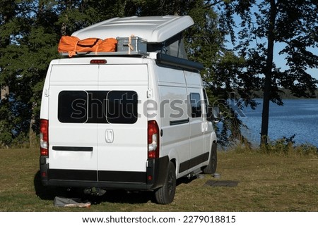 White camper van with pop-up roof on a  camping pitch of a natural campsite in Sweden.	