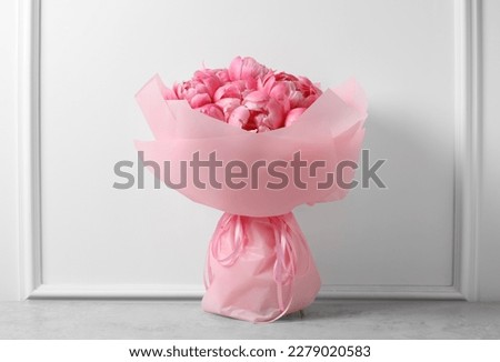 Bouquet of beautiful pink peonies on table near white wall
