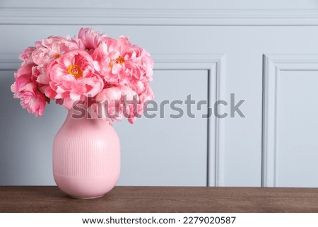 Beautiful bouquet of pink peonies in vase on wooden table near grey wall. Space for text