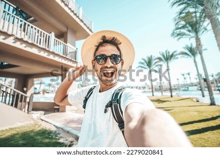 Happy tourist with backpack taking selfie on summer vacation - Delightful guy smiling at camera outside - Life style, technology and tourism concept