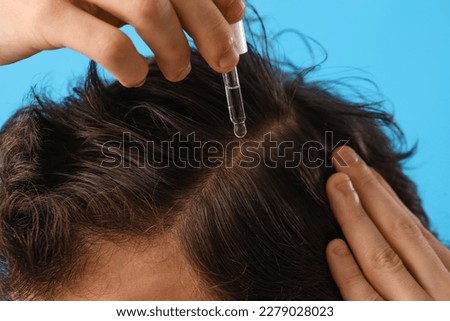Young man using serum for hair growth on blue background, closeup Royalty-Free Stock Photo #2279028023