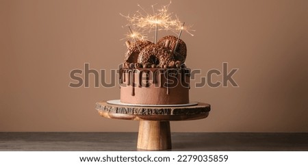 Sweet chocolate cake with sparklers on table against beige background
