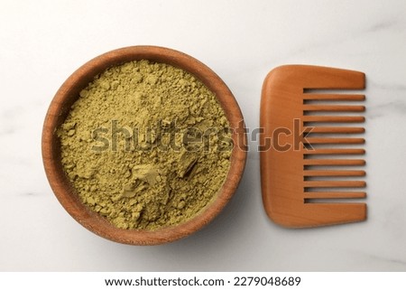 Bowl of henna powder and comb on white marble table, flat lay