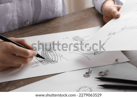 Jeweler drawing sketch of elegant earrings at wooden table, closeup