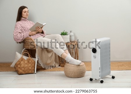 Woman reading book near modern portable electric heater indoors Royalty-Free Stock Photo #2279063755