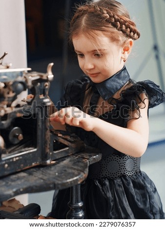 cute little girl with pigtail in a black dress prints on a retro typewriter. the concept of elegant clothes for children. cosplay.