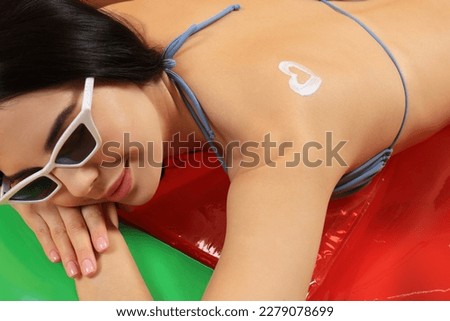 Young woman with sunglasses and heart drawn with sunscreen lying on inflatable mattress, closeup. Seasonal suntan
