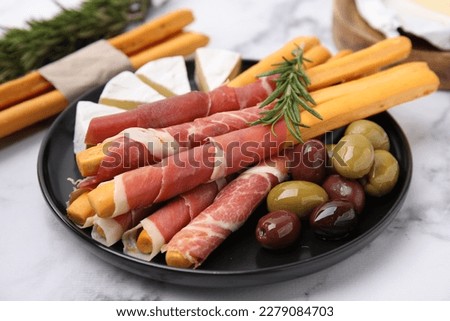 Delicious grissini sticks with prosciutto, cheese and olives on white marble table, closeup Royalty-Free Stock Photo #2279084703