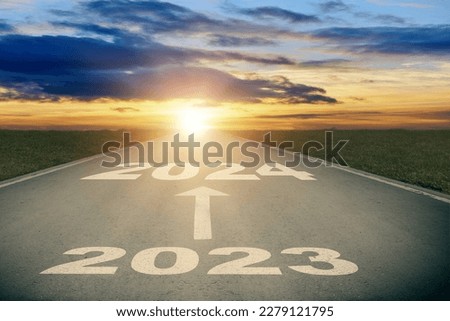 Asphalt road with white arrow sign and 2024 text goes to horizon. Sunshine on horizon and the road strigt away forward. Moving forward into new year concept. Clear and positive perspectives ahead.