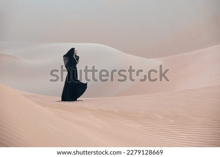 Beautiful young woman with a black abaya walking on the dunes in the desert. Royalty-Free Stock Photo #2279128669