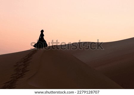 Silhouette of a beautiful young woman with a black abaya walking on the dunes in the desert.