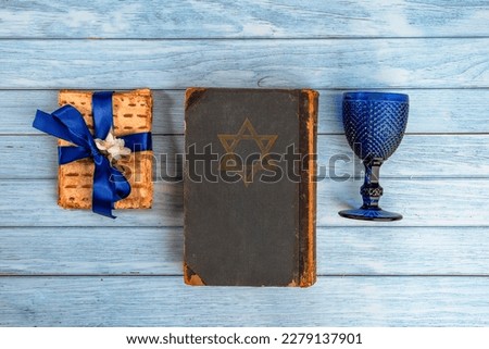 Pesah Jewish Passover holiday celebration concept. Matzah, wineglass, blooming jasmine, and religious book Torah with a Star of David. Blue wooden background with empty copy space.