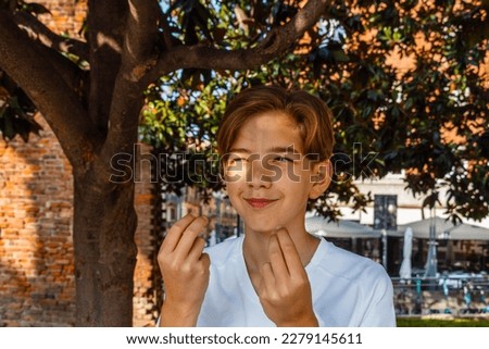Teenage boy doing italian hand gestures while standing under a tree. High quality photo