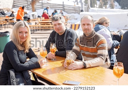 Happy family, enjoying ski holiday with children, sunny beautiful weather outdoors, people drinking aperol spritz on a sunny day