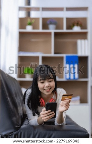 Asian young woman holding credit card in hand paying electronic money on remote online shopping at home on sofa vertical image