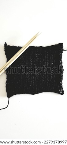 top view of black yarn swatch with wooden knitting needles on top