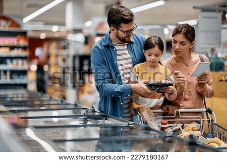 Little girl and her parents choosing groceries while shopping at supermarket. Copy space. Royalty-Free Stock Photo #2279180167