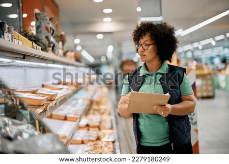 Female worker checking products in refrigerated section while working in supermarket. Royalty-Free Stock Photo #2279180249