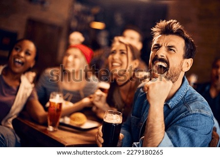 Young man screaming while watching sports game with his friends in a bar. Royalty-Free Stock Photo #2279180265