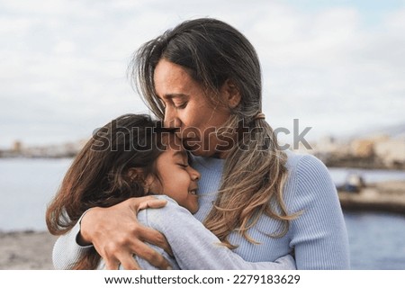 Latin mother and daughter having tender moment on the beach - Loving mom kissing her child outdoor - Family love concept