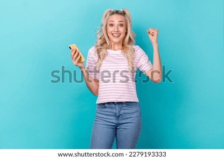 Photo of excited funny overjoyed awesome blonde curly hair girl hold phone fists up gambling victory jackpot isolated on blue color background