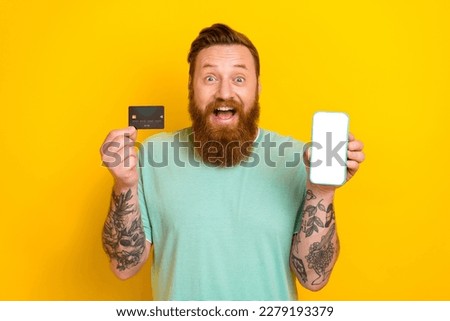Photo of young businessman shopaholic hold smartphone display tattooed hands debit card eshop display web menu isolated on yellow color background