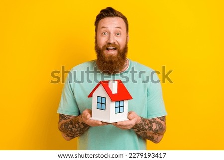 Photo of young surprised man red hair beard wear green t-shirt hold real estate relocation promo realtor agency isolated on yellow color background