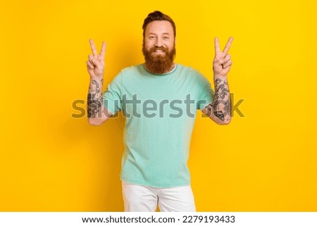 Portrait of glad nice guy tattoo artist wear stylish mint clothes demonstrate arms v-sign isolated on yellow color background