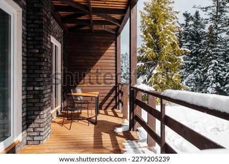 Two chairs and table standing at big wooden terrace in wooden house with winter forest around. Nature and vacation concept. Stock photo 