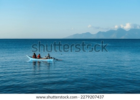 FloresIndonesia 20290808: A fishermen's boat crossing a calm sea near Maumere, Indonesia There are three men in one small, blue boat, one of them is paddling. Calm surface of the sea. Royalty-Free Stock Photo #2279207437