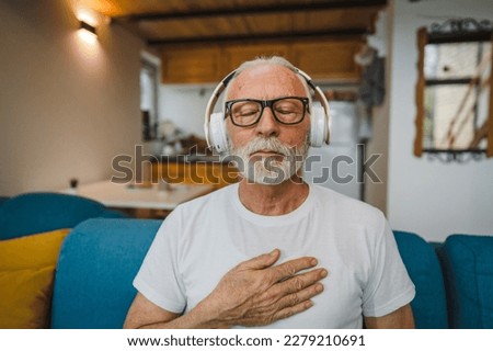 One man senior caucasian male eyes closed for guided training yoga or meditation while sitting at home with headphones self-care practice real people well-being inner peace and balance concept Royalty-Free Stock Photo #2279210691