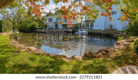 Small pond with grassy shore near the buildings with boat docks in Miami, Florida. Views from the shore under the tree at the front of a lake near the buildings at the background.